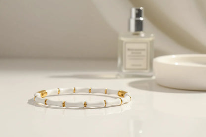White Bamboo bangle Bracelet resting on a glossy vanity surface with a perfume bottle softly blurred in the background, creating an elegant morning routine scene | Oria Jewel