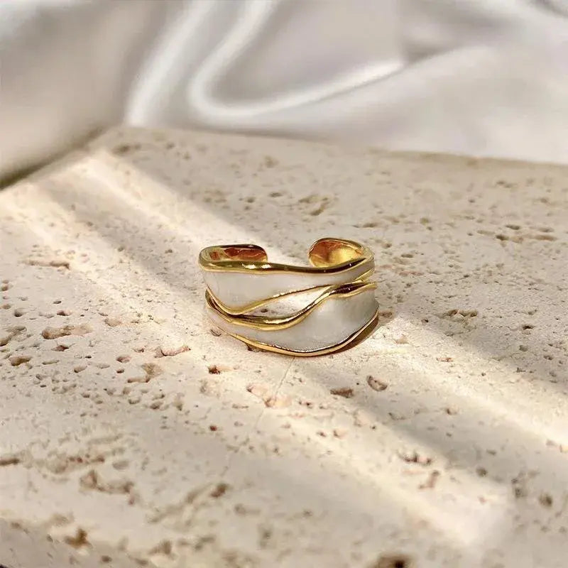 White Enamel Open Wave Ring product close-up on a textured stone surface, highlighting the open adjustable band and flowing gold wave lines over white enamel in soft natural light | OriaJewel
