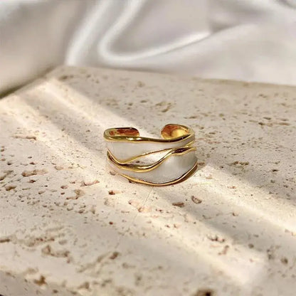 White Enamel Open Wave Ring product close-up on a textured stone surface, highlighting the open adjustable band and flowing gold wave lines over white enamel in soft natural light | OriaJewel