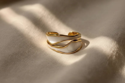 White Enamel Open Wave Ring close-up on beige fabric with soft light patterns, showing the curved gold wave lines and white enamel panels with an open adjustable fit | OriaJewel