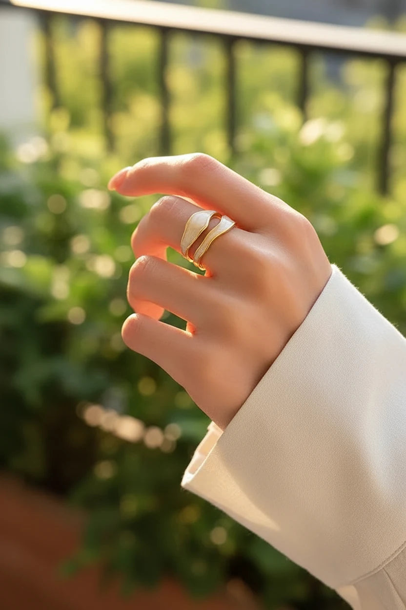 White Enamel Open Wave Ring worn outdoors with a blurred green background, golden-hour light emphasizing the gold-and-white wave layers and open adjustable ring shape | OriaJewel