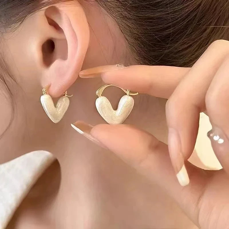 White Heart Huggie Hoop Earrings close-up worn on ear with hand detail | OriaJewel