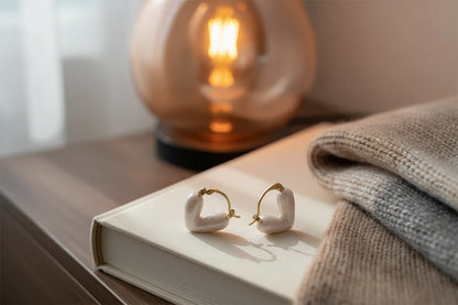 White Heart Huggie Hoop Earrings on book with warm lamp light | OriaJewel