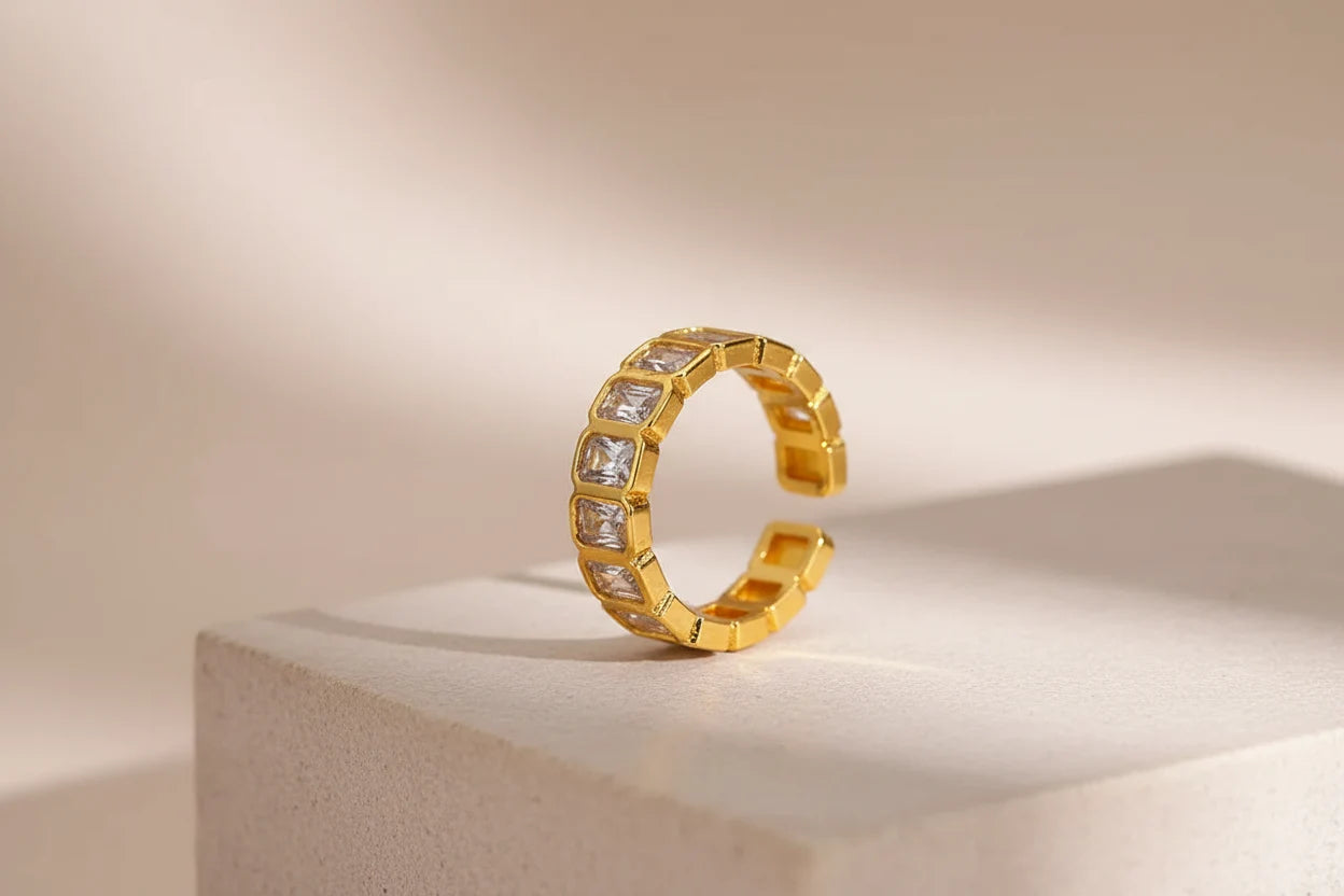 White stone band ring product close-up, open adjustable band with square clear stones, photographed on a beige pedestal with warm natural light and gentle shadows | OriaJewel