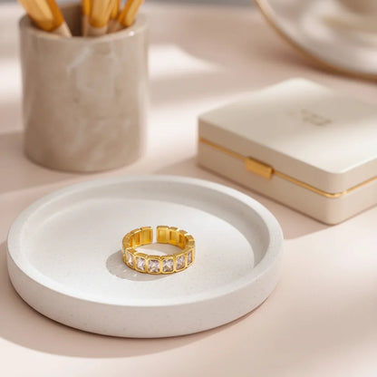 White stone band ring resting on a round white tray, styled with a neutral jewelry box and desk accessories in the background for a cozy, premium flat-lay feel | OriaJewel
