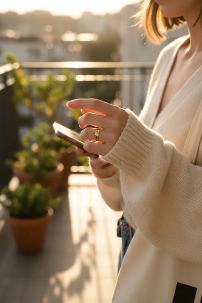 Wide Gold Band Ring worn while holding a phone on a sunlit balcony, golden hour glow catching the wide band ring shine with a soft city background blur | OriaJewel