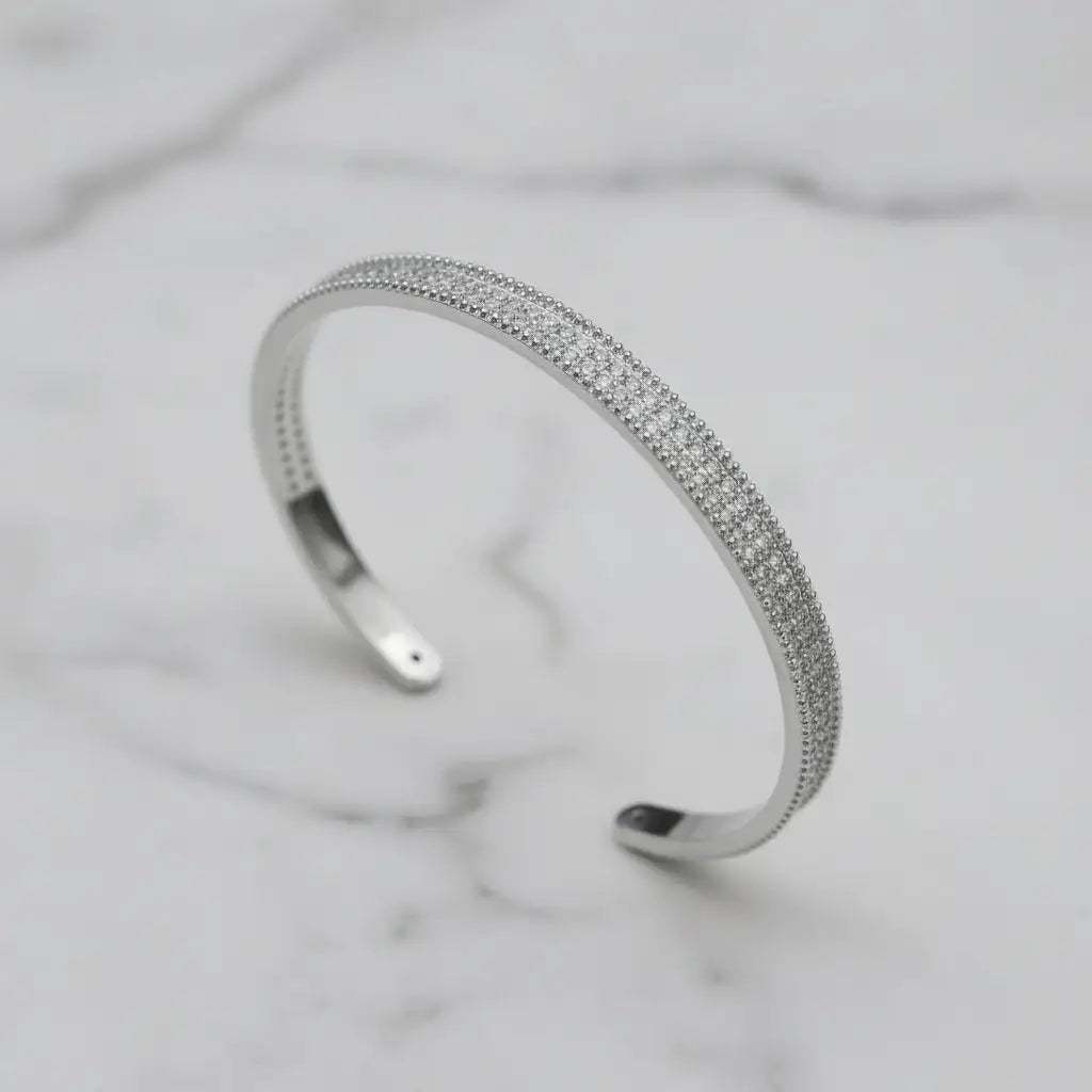 Minimalist close-up of the silver Xaria Pavé Wrist Cuff with three rows of sparkling crystals displayed on a white marble background, showing its open cuff design and refined texture | Oria Jewel