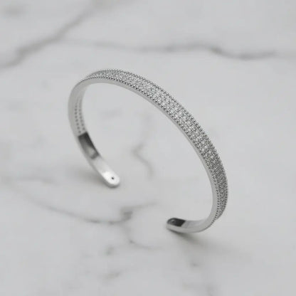 Minimalist close-up of the silver Xaria Pavé Wrist Cuff with three rows of sparkling crystals displayed on a white marble background, showing its open cuff design and refined texture | Oria Jewel