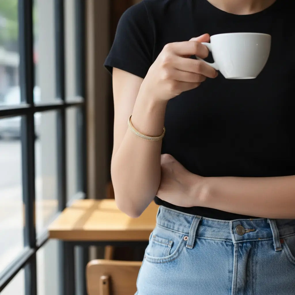 Casual café scene with woman in black tee and jeans holding a coffee cup, styling the minimalist Xaria Pavé Wrist Cuff | Oria Jewel

