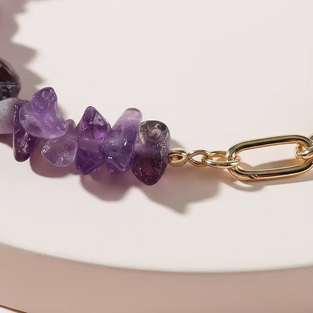 Macro close-up of irregular purple stones and a polished gold link connection on an amethyst bead bracelet, showing the natural variations in the crystals and the smooth finish of the chain detail | Oria Jewel