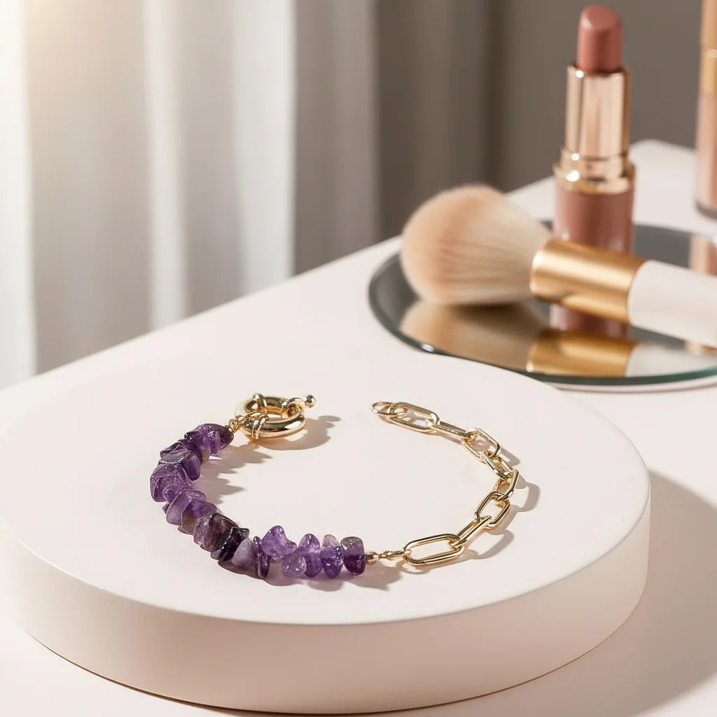 Vanity scene with a purple amethyst bead bracelet lying on a round white display tray, surrounded by makeup brushes and lipstick, with warm morning light emphasizing the sparkle of the stones and gold chain | Oria Jewel