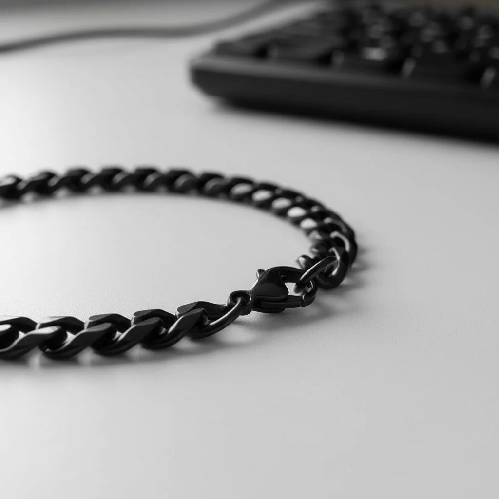 Macro side view of a black chain bracelet laid on a clean desk near a computer keyboard, emphasizing the smooth, curved links and modern office-ready style of the black chain bracelet | Oria Jewel