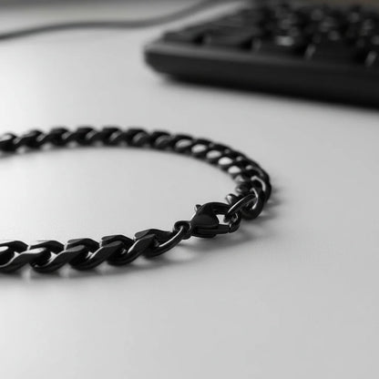 Macro side view of a black chain bracelet laid on a clean desk near a computer keyboard, emphasizing the smooth, curved links and modern office-ready style of the black chain bracelet | Oria Jewel