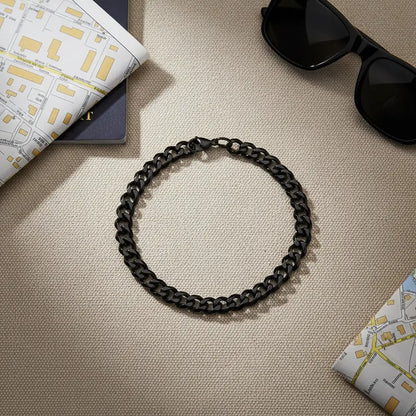 Travel-inspired flat lay featuring a black chain bracelet arranged on textured fabric with sunglasses, city maps and a passport, showcasing the bracelet as a versatile everyday accessory for trips and adventures | Oria Jewel