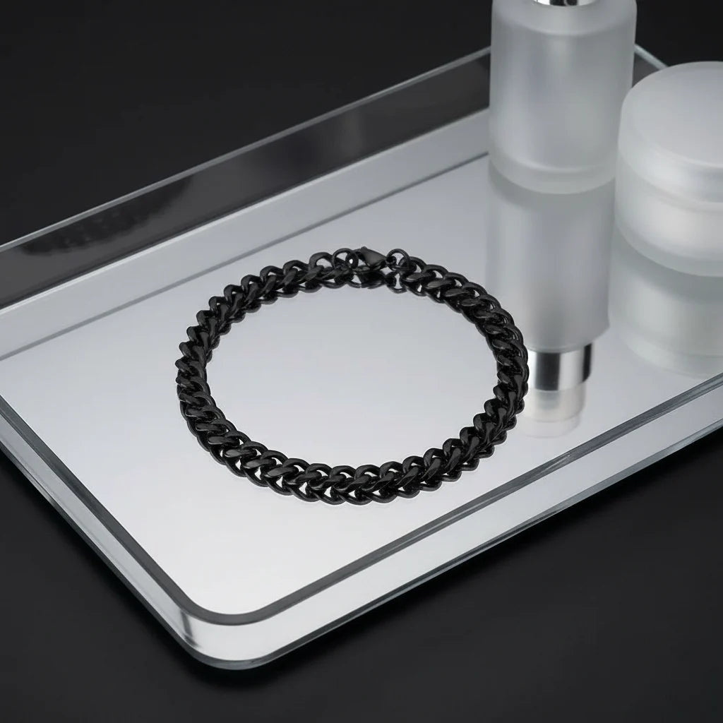 Elegant display of a black chain bracelet on a mirrored tray with frosted cosmetic jars in the background, reflections highlighting the shiny black links and refined, minimalist design of the chain bracelet | Oria Jewel