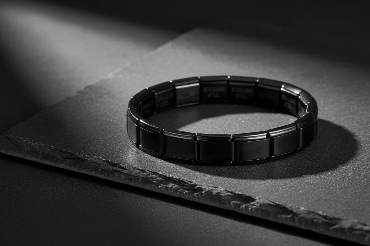 Dramatic studio shot of a single bracelet from the black stainless steel stretch bracelets collection displayed on a dark stone slab, highlighted by a focused beam of light that emphasizes its smooth, segmented links and glossy finish | Oria Jewel