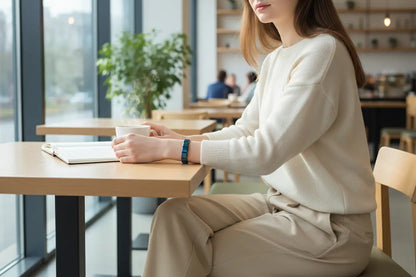 Casual outdoor scene of a woman working on a laptop on a park bench at golden hour, with a modern blue stainless steel stretch bracelets on her wrist standing out against her striped top and blue jeans | Oria Jewel