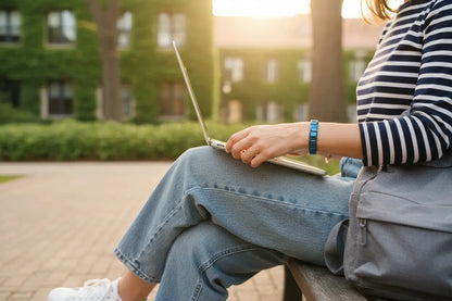 Casual outdoor scene of a woman working on a laptop on a park bench at golden hour, with a modern blue stainless steel stretch bracelets on her wrist standing out against her striped top and blue jeans | Oria Jewel