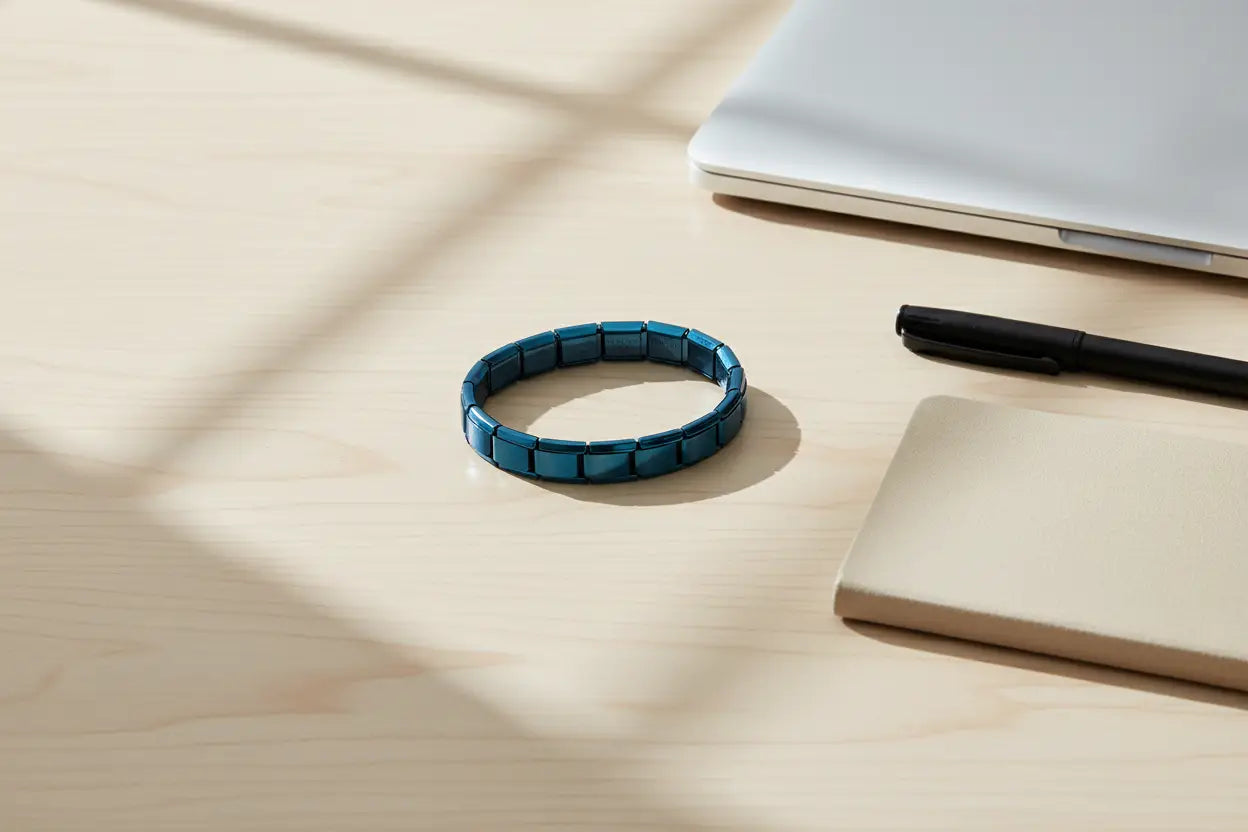 Overhead desk flat lay featuring a laptop, pen, and notebook with a neatly arranged blue stainless steel stretch bracelets in the center, bathed in window light to showcase its professional, everyday-wear style | Oria Jewel