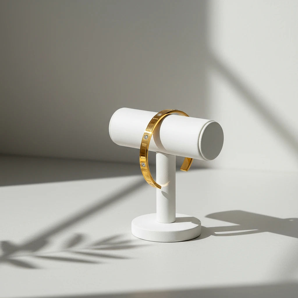 Minimalist gold crystal cuff bracelet displayed on a white T-bar stand, lit by soft natural light with plant shadows falling across a clean neutral background | Oria Jewel