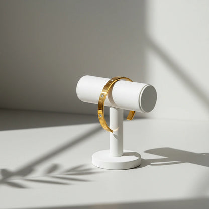 Minimalist gold crystal cuff bracelet displayed on a white T-bar stand, lit by soft natural light with plant shadows falling across a clean neutral background | Oria Jewel