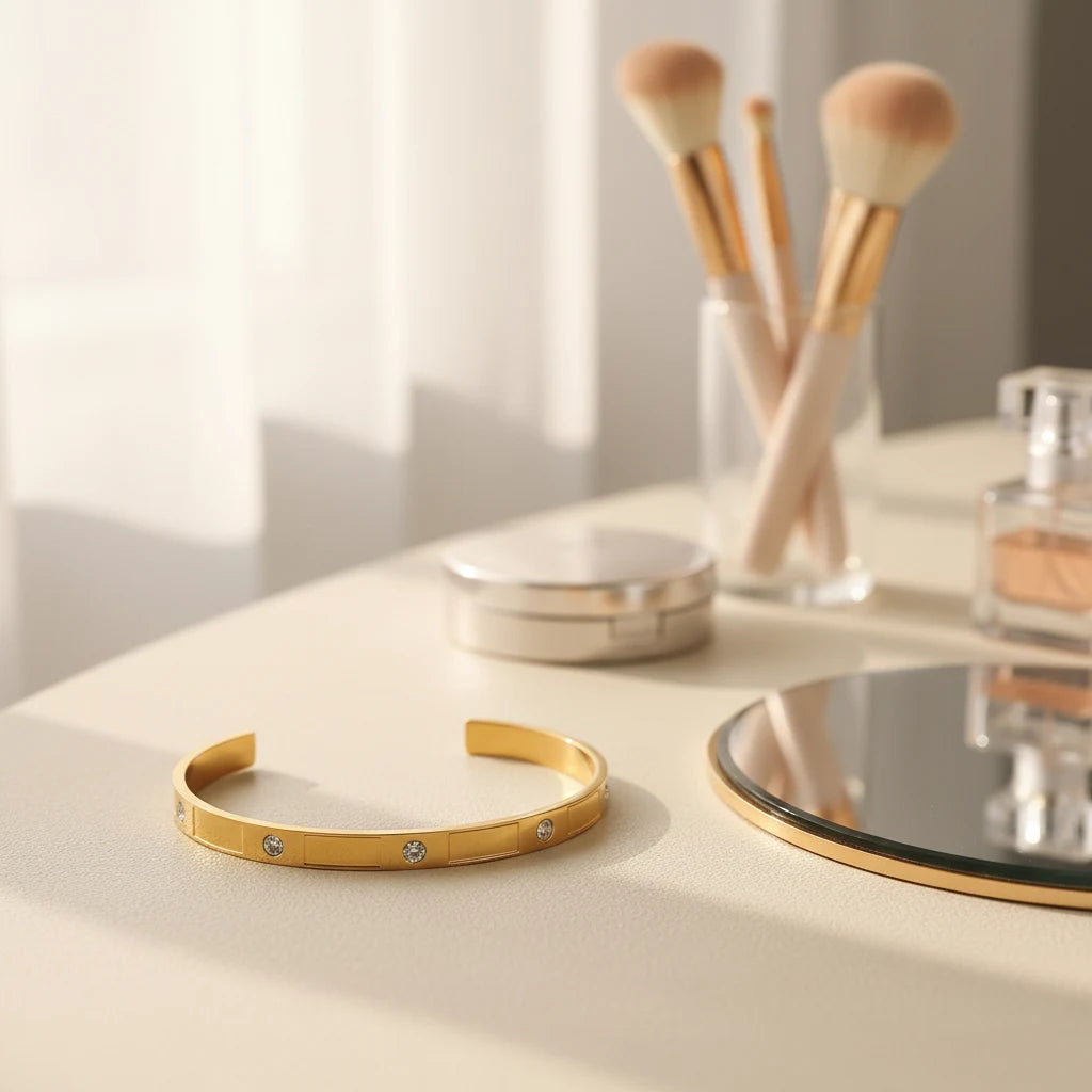 Gold crystal cuff bracelet resting on a vanity table beside makeup brushes, compact and mirror, in warm morning light for an elegant getting-ready scene | Oria Jewel
