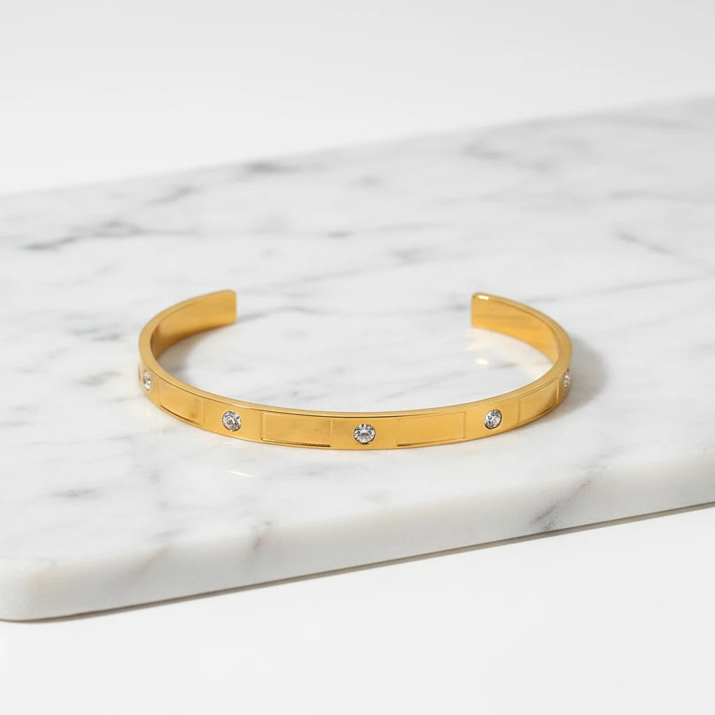 Close-up of a gold crystal cuff bracelet displayed on a white marble tray, highlighting its sleek shape and sparkling round stones | Oria Jewel