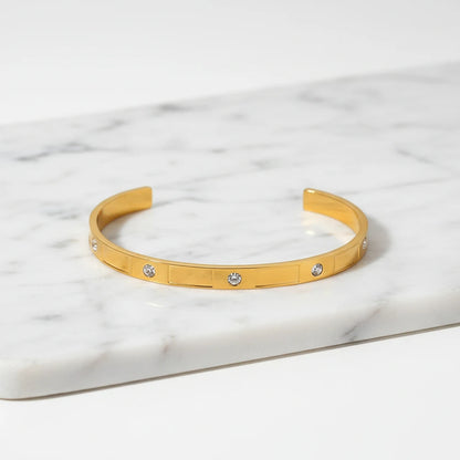 Close-up of a gold crystal cuff bracelet displayed on a white marble tray, highlighting its sleek shape and sparkling round stones | Oria Jewel