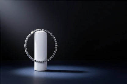 Dramatic studio shot of a cz tennis bracelet standing upright around a white cylinder pedestal against a deep black background, stones sparkling under a focused spotlight for an elevated, luxurious feel | Oria Jewel