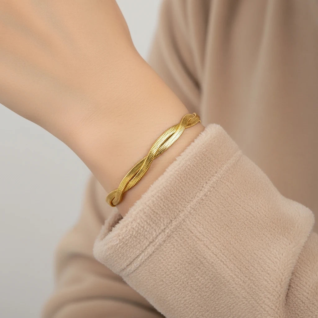 Close-up of a wrist wearing a twisted double chain gold bracelet styled with a soft beige sweater sleeve against a neutral background | Oria Jewel