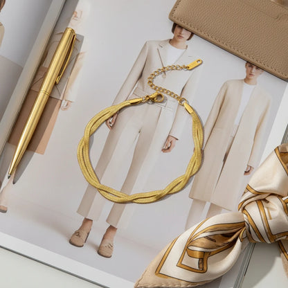 Fashion flat lay of a double chain gold bracelet placed on a minimalist style magazine with neutral outfits, beside a gold pen and patterned silk scarf | Oria Jewel