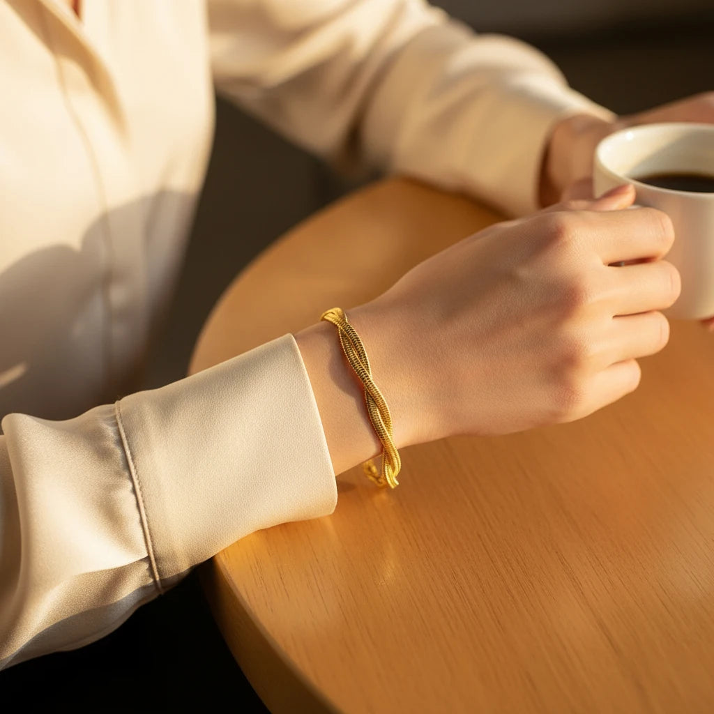 Warm lifestyle close-up of a hand holding a coffee cup on a wooden table, highlighting the sleek double chain gold bracelet catching the sunlight | Oria Jewel