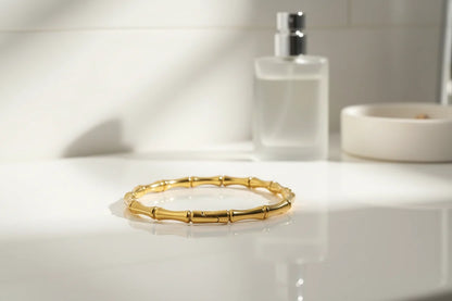 Gold Bamboo bangle Bracelet displayed on a white bathroom vanity next to a perfume bottle and ceramic dish, styled as an elegant morning getting-ready setup | Oria Jewel
