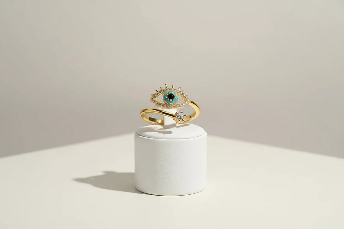 gold Evil Eye Ring displayed upright on a small white pedestal, clean minimal backdrop, crisp studio light highlighting the eye centerpiece and gold band | OriaJewel