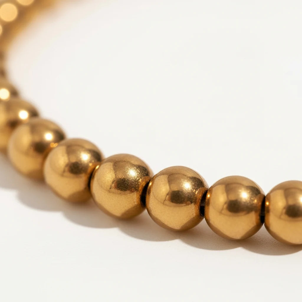 Close-up macro shot of a gold beaded stretch bracelet showing the smooth, reflective round beads and rich 18K gold tone on a clean white background | Oria Jewel