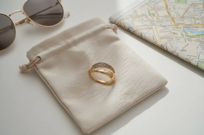 Minimal travel flat lay with sunglasses, map, and pouch, featuring a gold bypass ring placed neatly on a soft drawstring bag | OriaJewel