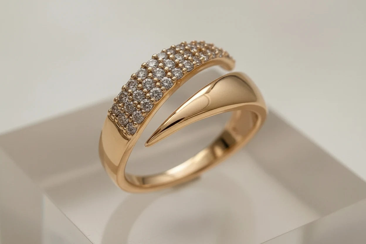 Detailed close-up of a modern gold bypass ring on a clear display block, showing the smooth crossover band and pavé-set top curve | OriaJewel
