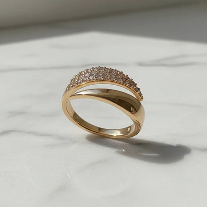 Product shot on white marble with natural shadow, featuring a glossy curved gold bypass ring and its pavé sparkle in daylight | OriaJewel