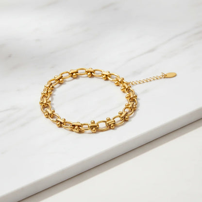 Detailed product image of a gold chain link bracelet arranged in a neat circle on a white marble surface, showing the textured links and delicate extender chain | Oria Jewel