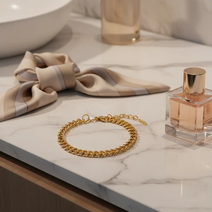 Elegant gold curb chain bracelet resting on a marble vanity beside a silk scarf and perfume bottle for a chic styling look | Oria Jewel