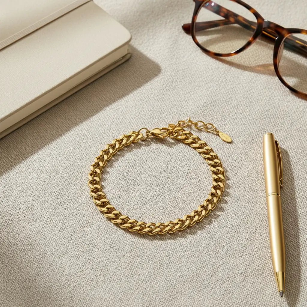 Gold curb chain bracelet laid flat on textured neutral fabric next to a notebook, glasses, and pen for a workday aesthetic | Oria Jewel