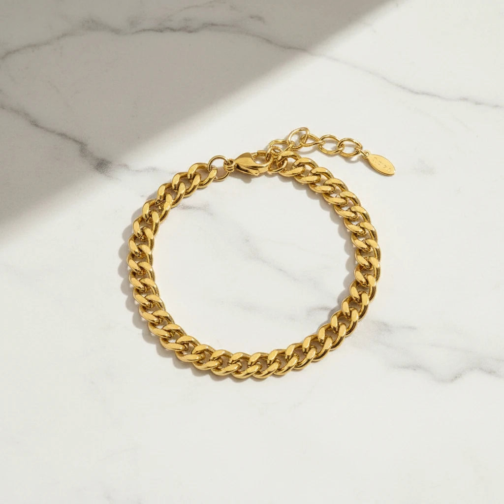 Classic gold curb chain bracelet arranged in a circle on white marble with diagonal sunlight creating modern, clean shadows | Oria Jewel