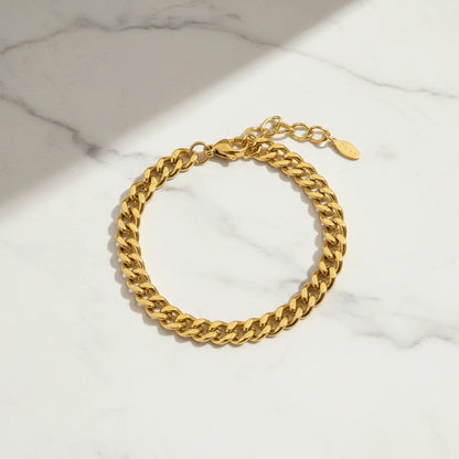Classic gold curb chain bracelet arranged in a circle on white marble with diagonal sunlight creating modern, clean shadows | Oria Jewel
