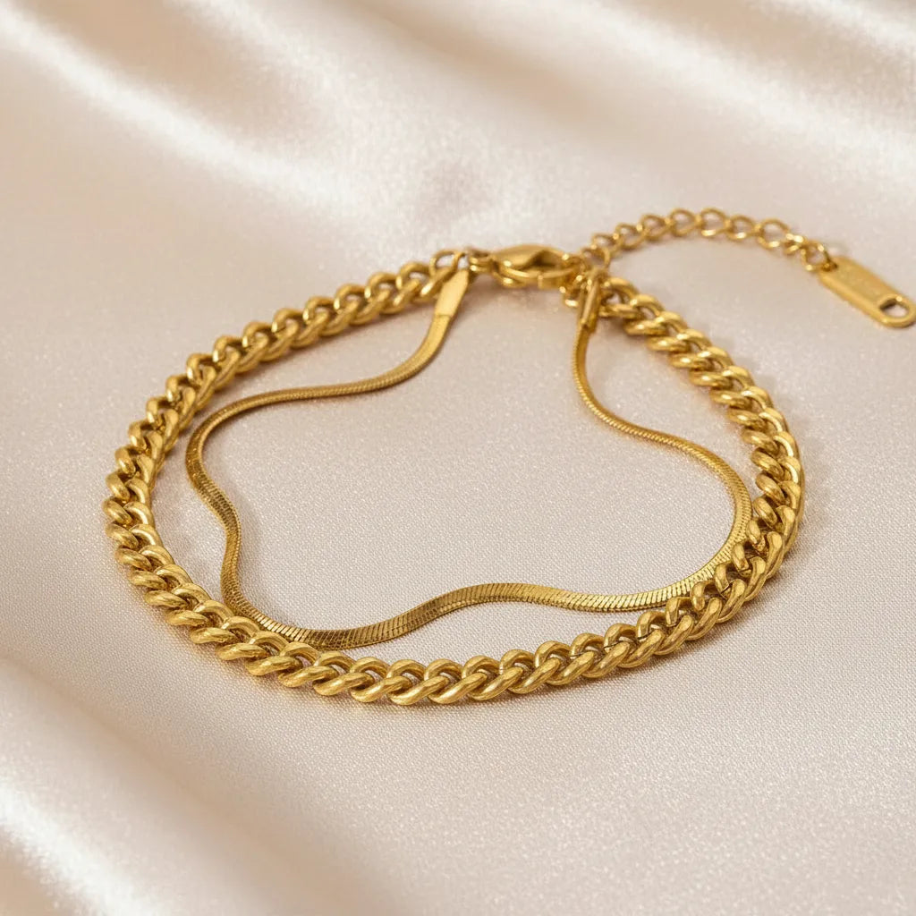 Refined gold double chain bracelet arranged on champagne satin fabric, emphasizing its fluid drape and polished links | Oria Jewel