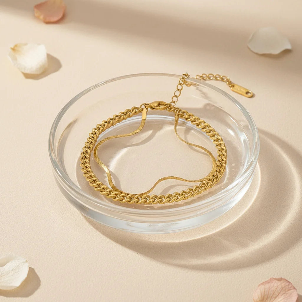 Elegant gold double chain bracelet placed inside clear glass dish with petals around, creating a soft romantic vibe | Oria Jewel