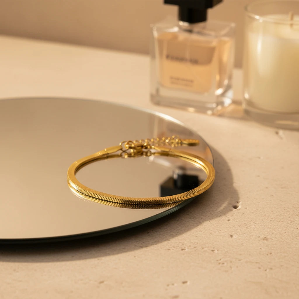 Gold herringbone chain bracelet resting on a round mirror tray beside perfume bottle and candle, creating a cozy vanity styling scene | Oria Jewel