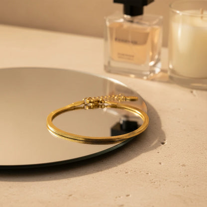 Gold herringbone chain bracelet resting on a round mirror tray beside perfume bottle and candle, creating a cozy vanity styling scene | Oria Jewel