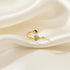 gold open heart ring with pavé crystal heart tip and smooth heart end on soft ivory satin folds, macro product photo | Oria Jewel