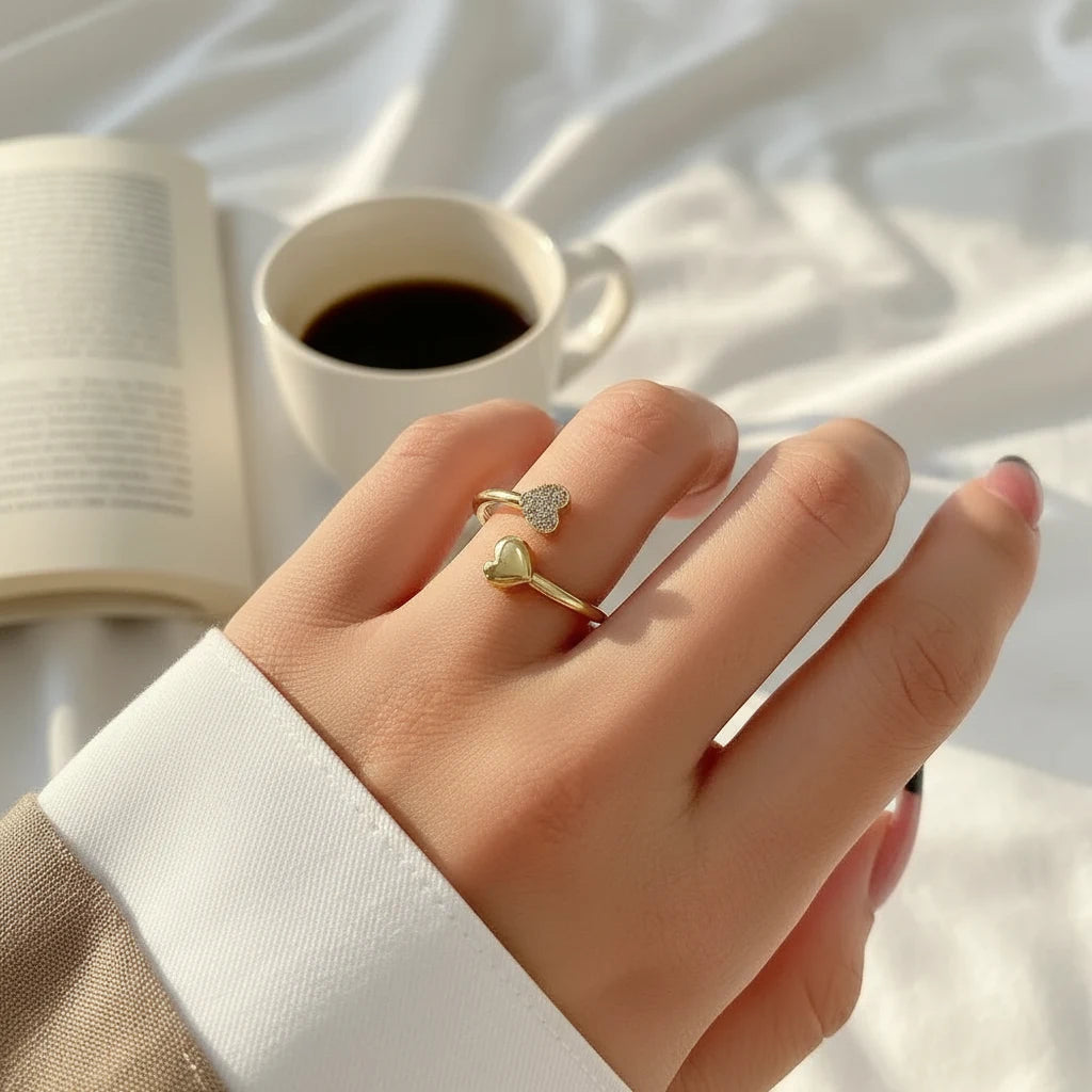 gold open heart ring worn on finger, open adjustable design with one pavé heart and one polished heart, coffee cup and book lifestyle scene | Oria Jewel