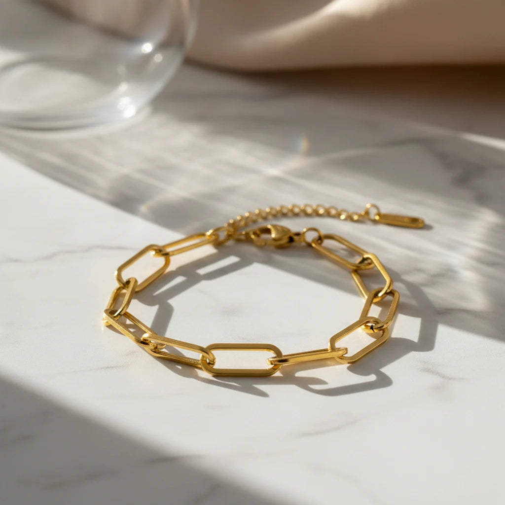 Minimal studio shot of a gold paperclip chain bracelet with extender chain resting on white marble in soft sunlight | Oria Jewel